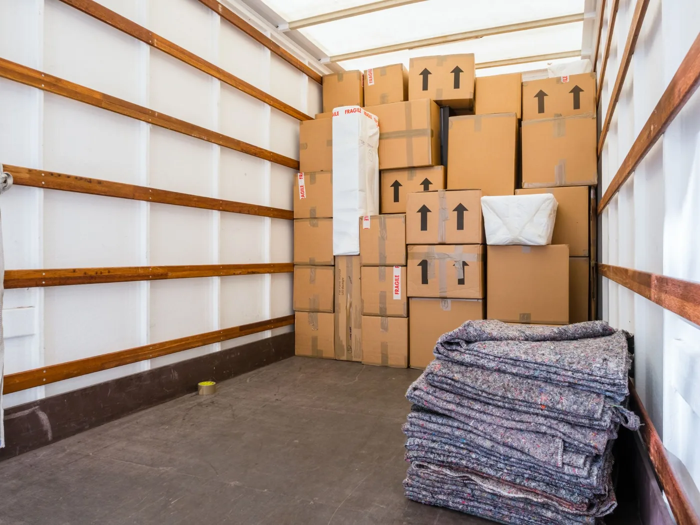 Boxes marked FRAGILE with upward arrows stacked inside a moving truck beside padded blankets