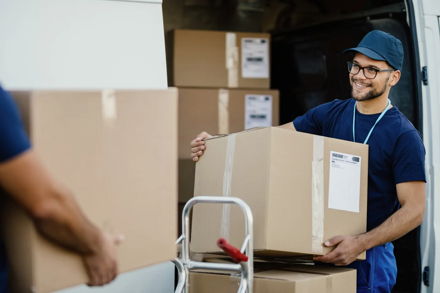 A mover smiling as he lifts a labelled box down from the back of a loaded van