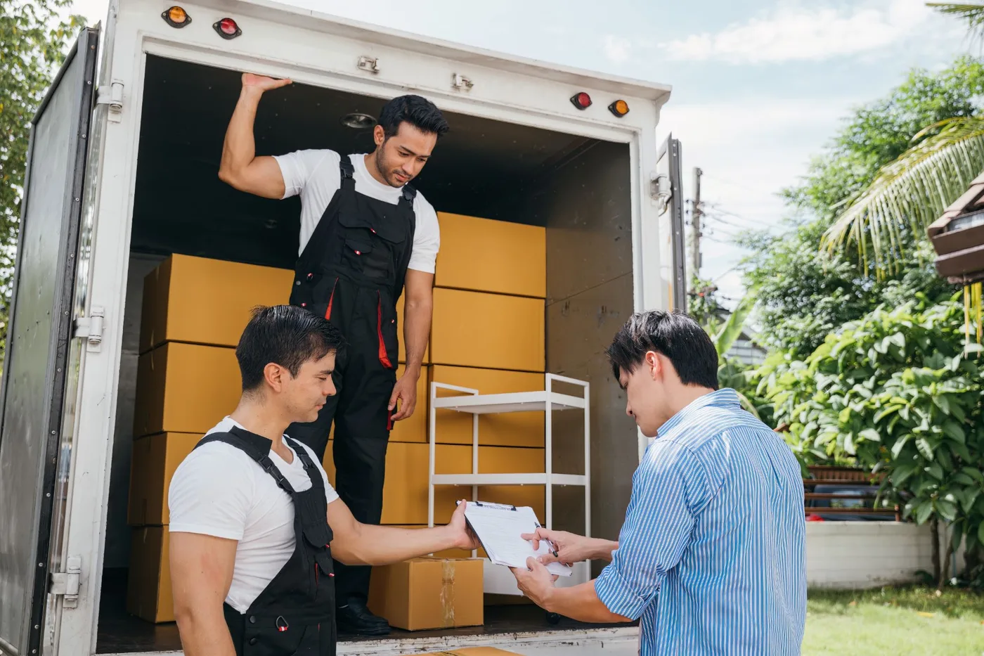 Two movers and a customer checking paperwork against boxes at the back of a moving truck