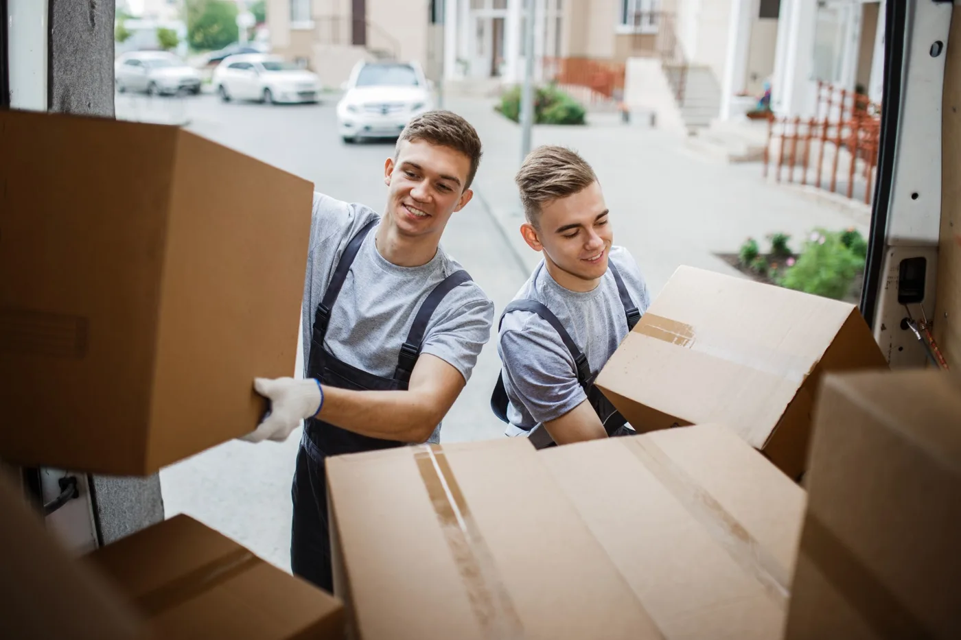 Two movers lifting cardboard boxes into the back of a van on a residential street