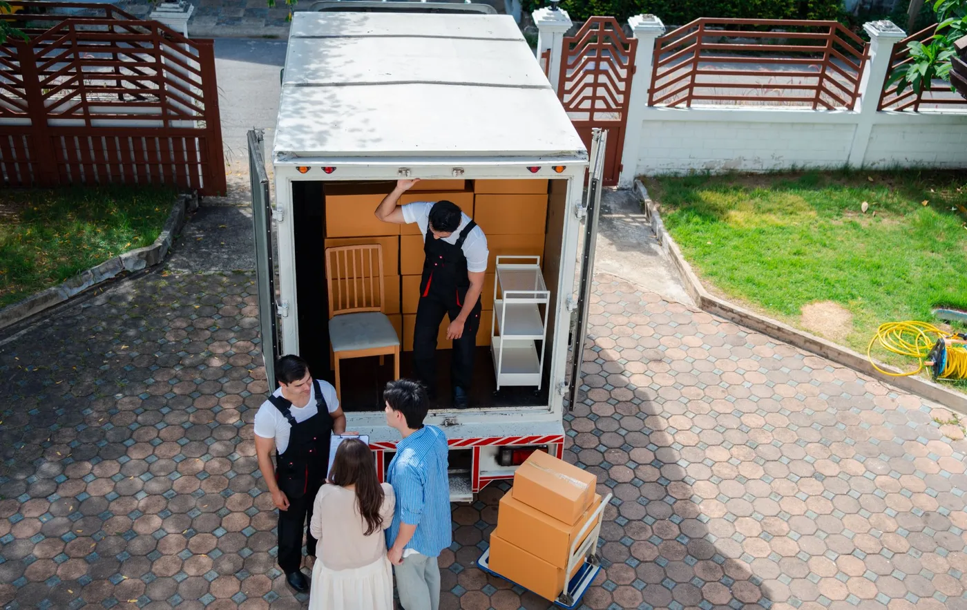 Overhead view of a moving truck in a driveway, movers loading furniture while a couple checks a list