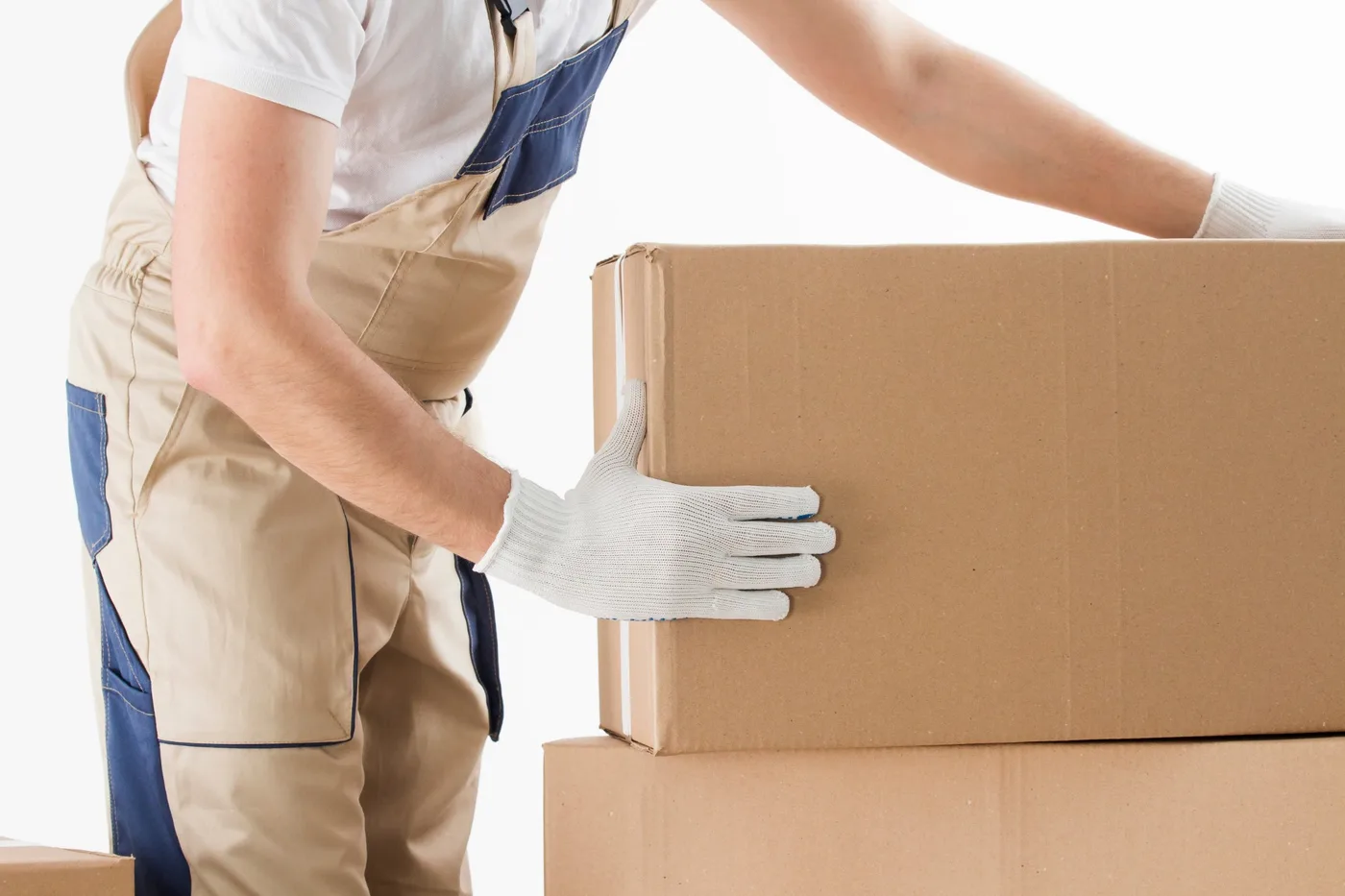A mover in work gloves and overalls stacking sealed cardboard boxes