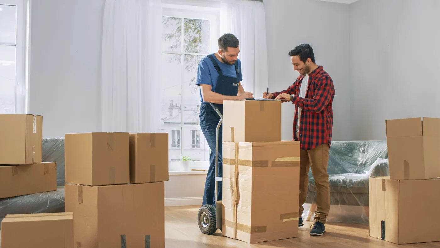 A customer signing moving paperwork on a clipboard beside a hand truck stacked with boxes