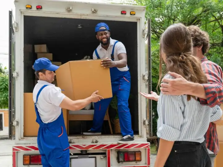 Two movers handing a box down from a moving truck while a couple watches